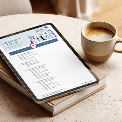 A tablet on a cozy table displays the intraMuse Creative Marketing Audit Checklist beside a latte and notebook, showing a detailed branding and marketing review worksheet for small businesses.