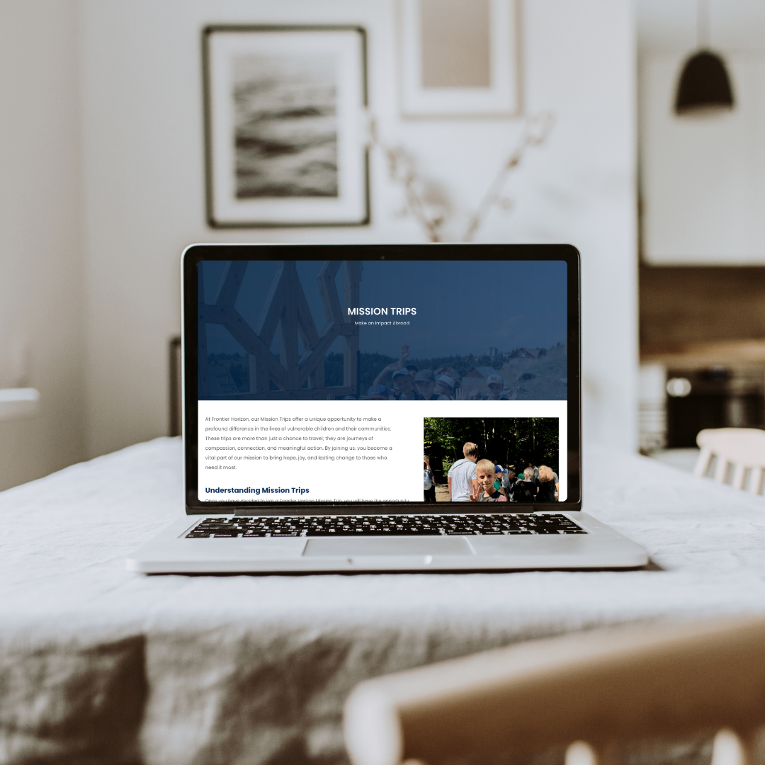 Laptop on a table showing the Frontier Horizon Mission Trips webpage, set in a cozy home interior environment.