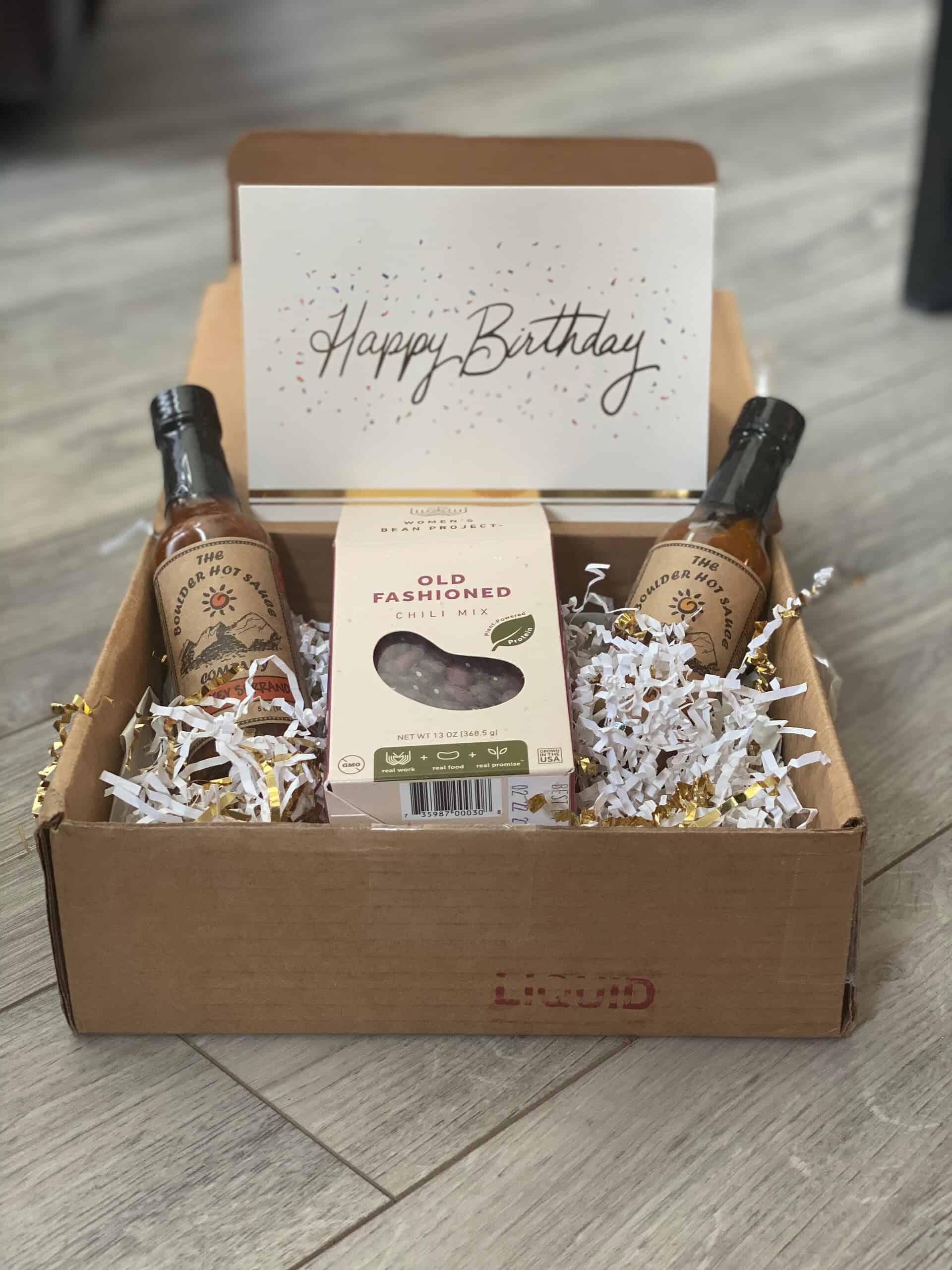 GWM- 2020 Birthday Box Birthday gift box from Generosity Wealth Management featuring two bottles of Boulder Hot Sauce, a box of old-fashioned chili mix, and a “Happy Birthday” card displayed on top.