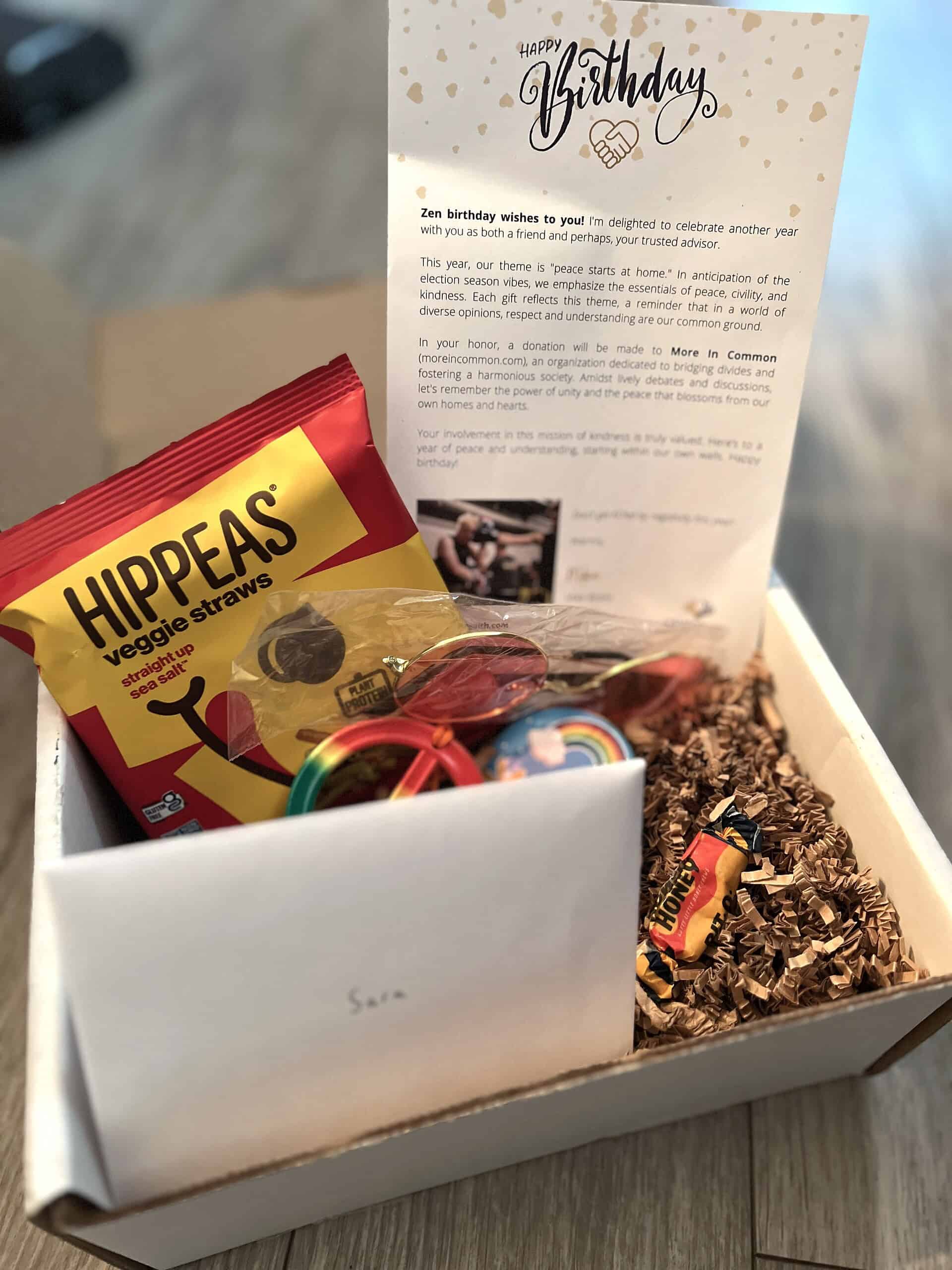 GWM- 2024 Birthday Box Generosity Wealth Management birthday gift box with Hippeas veggie straws, colorful trinkets, candy, and a printed note about a donation to More In Common, an organization promoting unity and understanding.