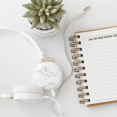 A minimalist workspace flat lay featuring an open notebook titled “New Year Brand Alignment Reset,” a cup of coffee, white headphones, a succulent plant, and a pencil on a bright white desk, representing intentional brand planning and reflection.